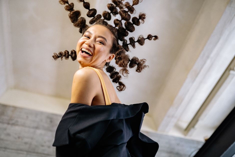 A woman laughing with unique curly hairstyle posing indoors, showcasing joy and style.