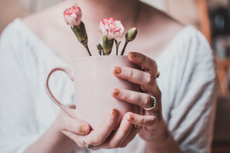 Aesthetic pink carnation buds in a ceramic mug, gently held by a woman with glittery nails