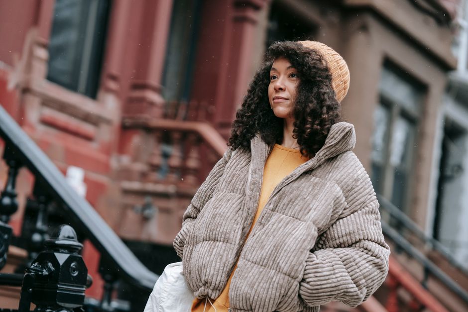 African American female with curly hair in outerwear with hands in pockets looking forward