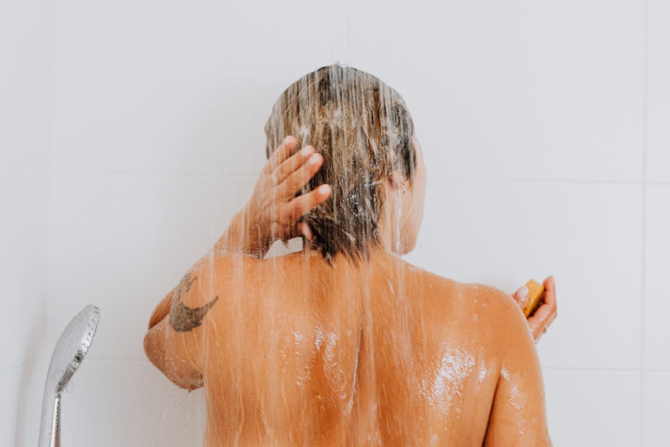 Rear view of a woman rinsing hair under shower, capturing an intimate and refreshing moment indoors.