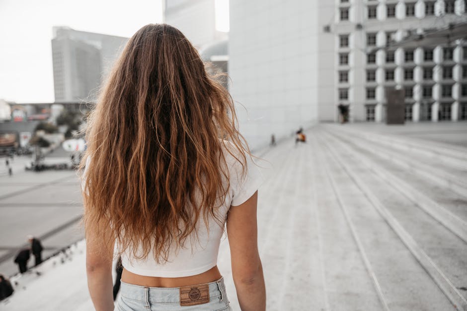 Woman with long brown hair walking up concrete steps in an urban setting.