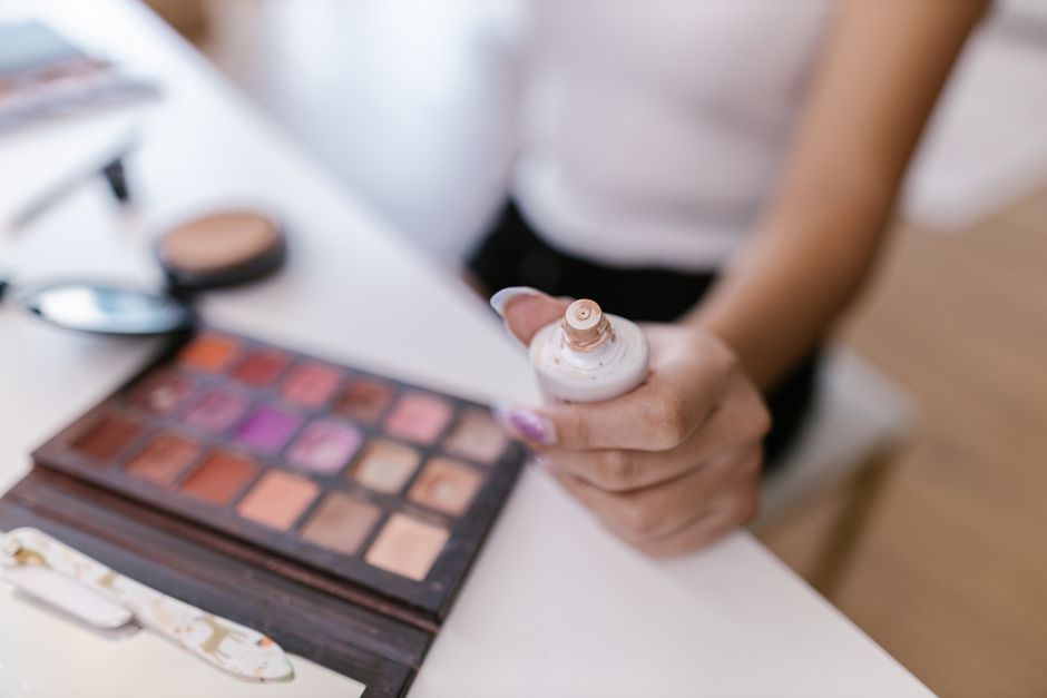 Close-up of a person holding foundation bottle with colorful makeup palette in focus.