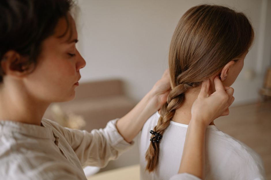 Close-up of a woman braiding another woman's hair indoors, evoking tranquility.