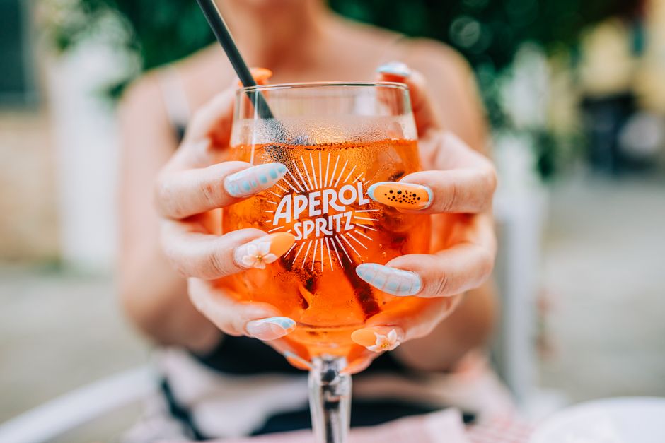Close-up of a woman enjoying an Aperol Spritz cocktail outdoors on a sunny day, showcasing