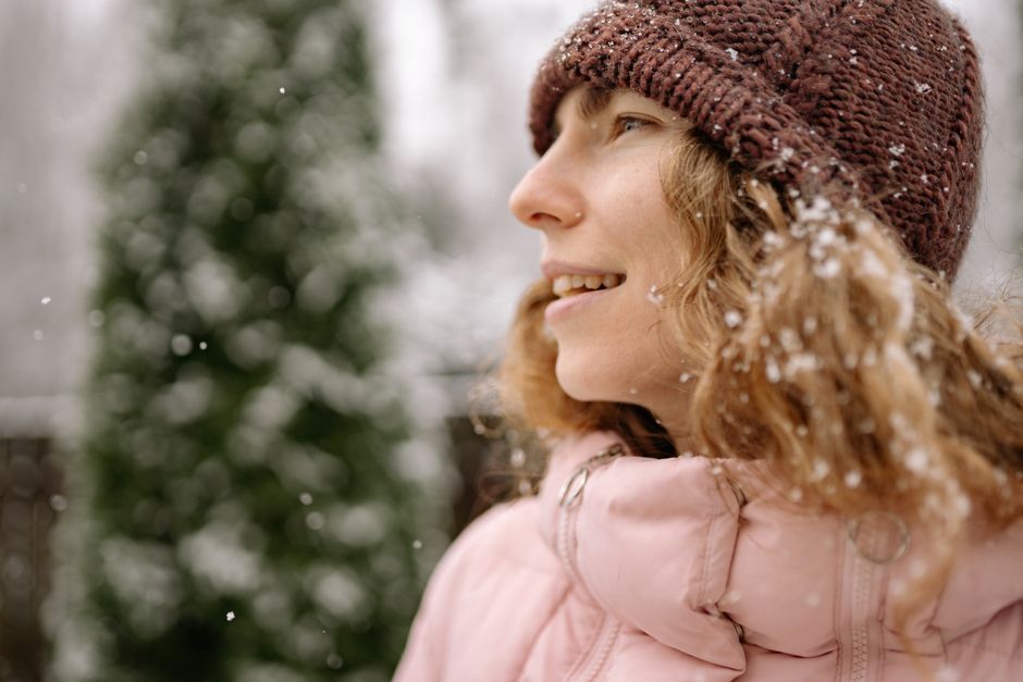 Close-up of a woman wearing a beanie and pink coat while enjoying a snowy winter day outsi