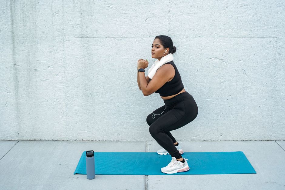 Confident woman doing squats on a yoga mat with a water bottle nearby. Fitness and lifesty