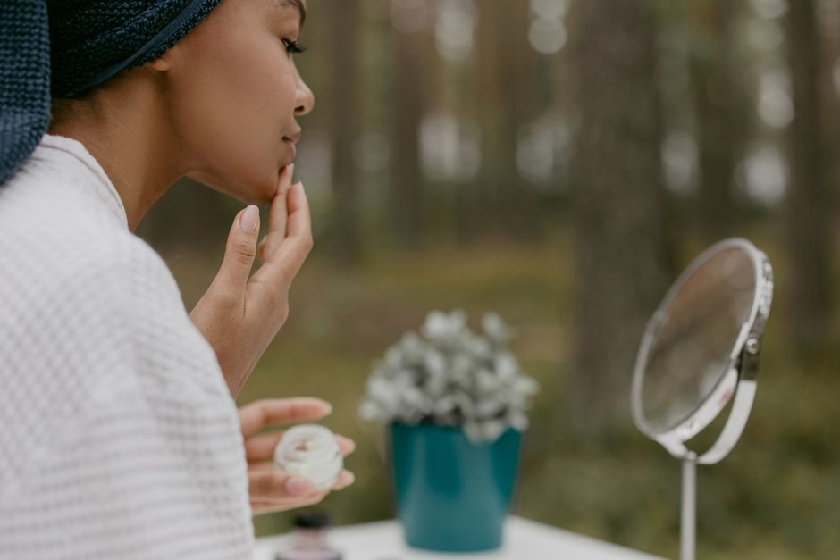 Woman enjoying skincare routine in serene forest setting. Self-care, beauty, and relaxation outdoors.