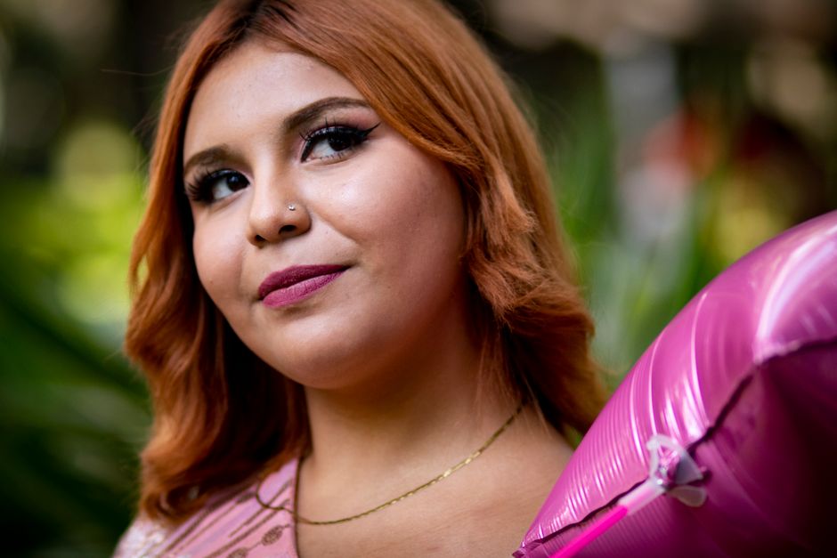 A cheerful young woman with red hair holding a pink balloon outdoors, enjoying a sunny day.