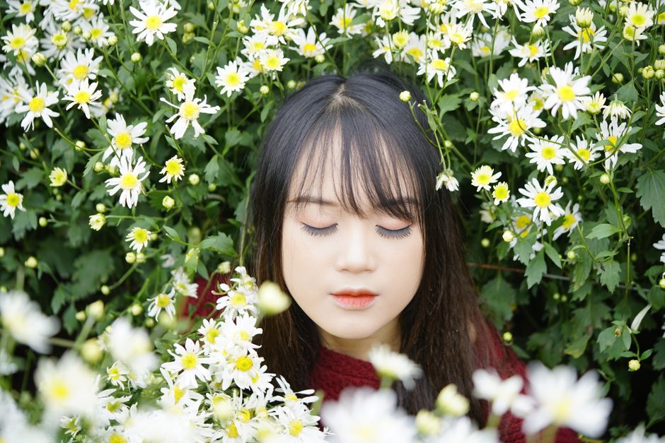 Concentrated ethnic female adolescent with makeup and closed eyes among blossoming white flowers in garden