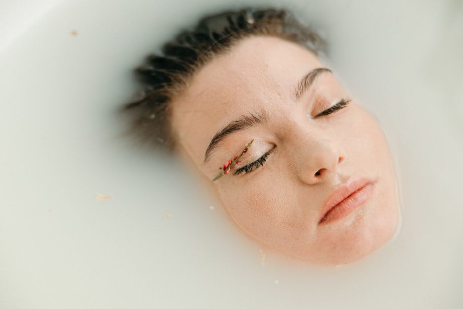 Close-up of a woman peacefully soaking in a milk bath adorned with floral elements.