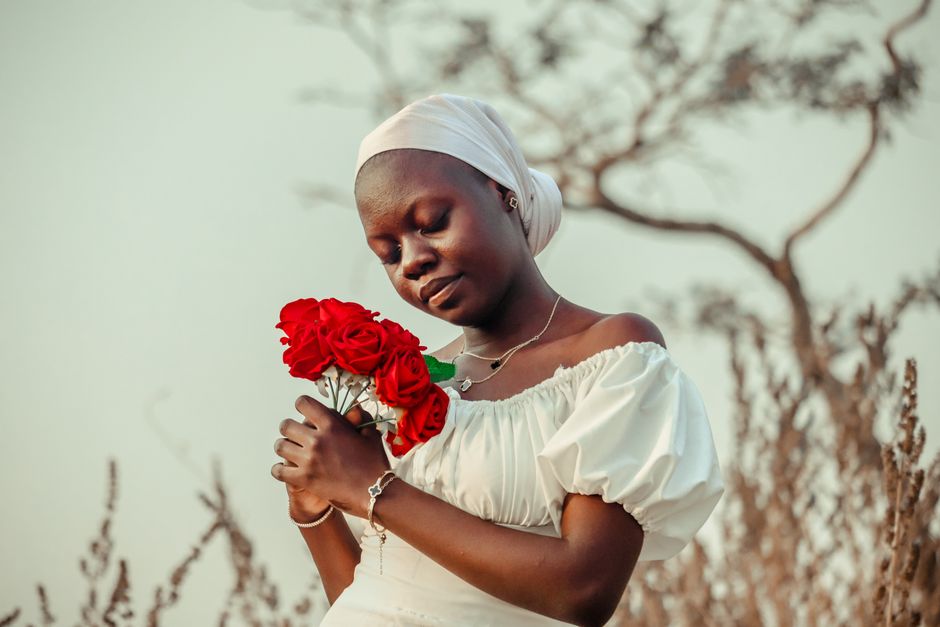 A woman in white holding red roses in a peaceful outdoor setting.
