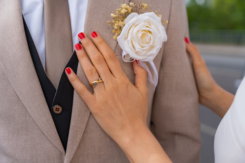 Close-up of a groom's suit with floral boutonniere and bride's hand showing wedding ring.