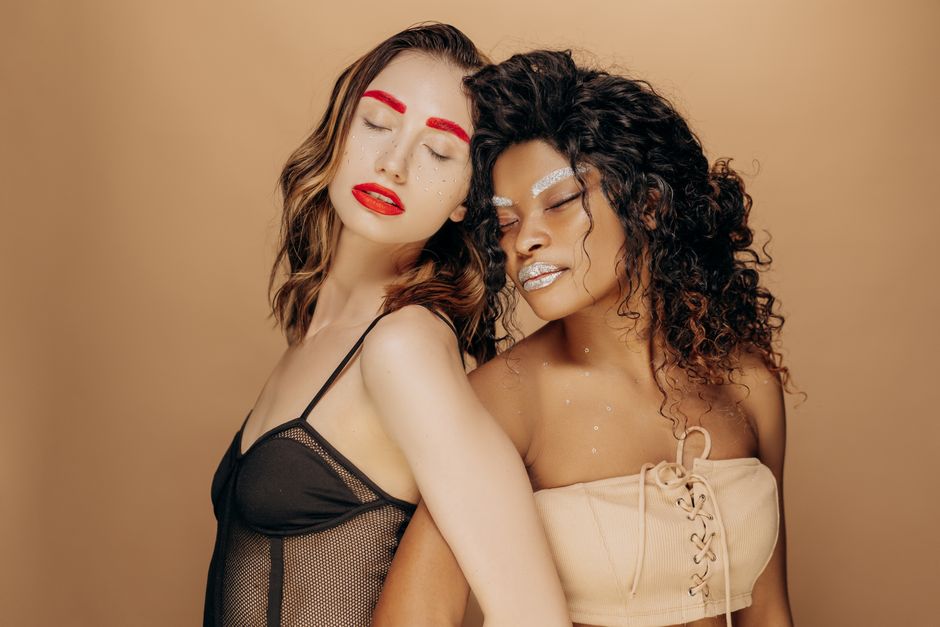 Two women wearing vivid creative makeup posing with eyes closed.