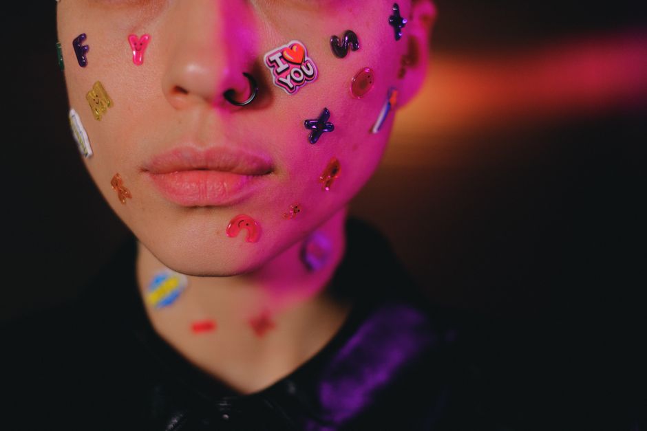 Crop unemotional female with many multicolored stickers on face standing in dark studio