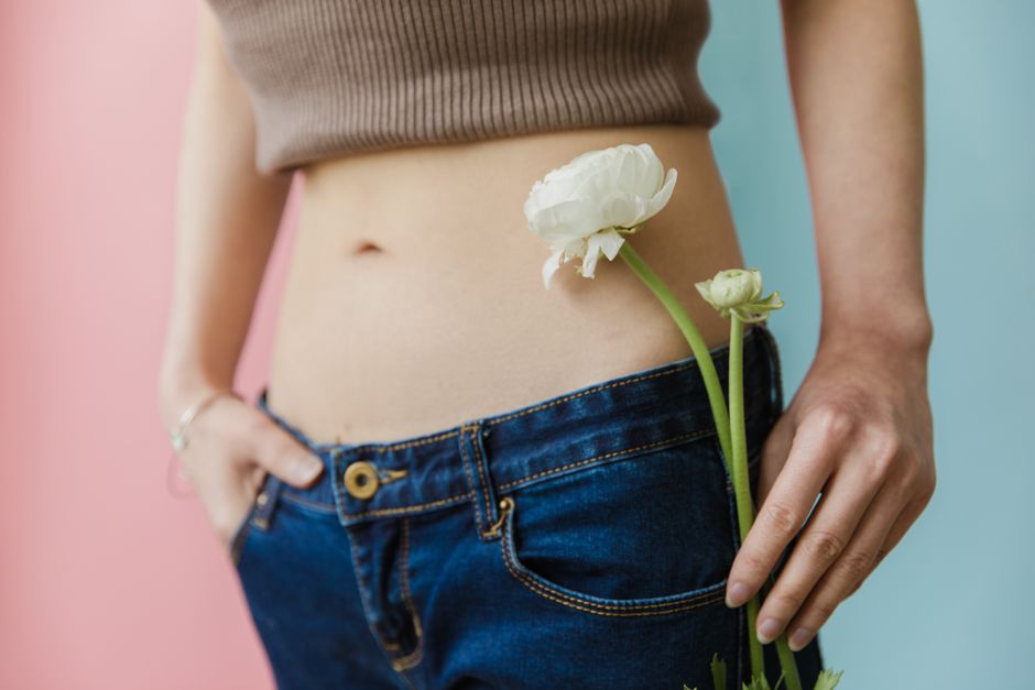 Close-up of a woman in a brown top and jeans holding a white flower.
