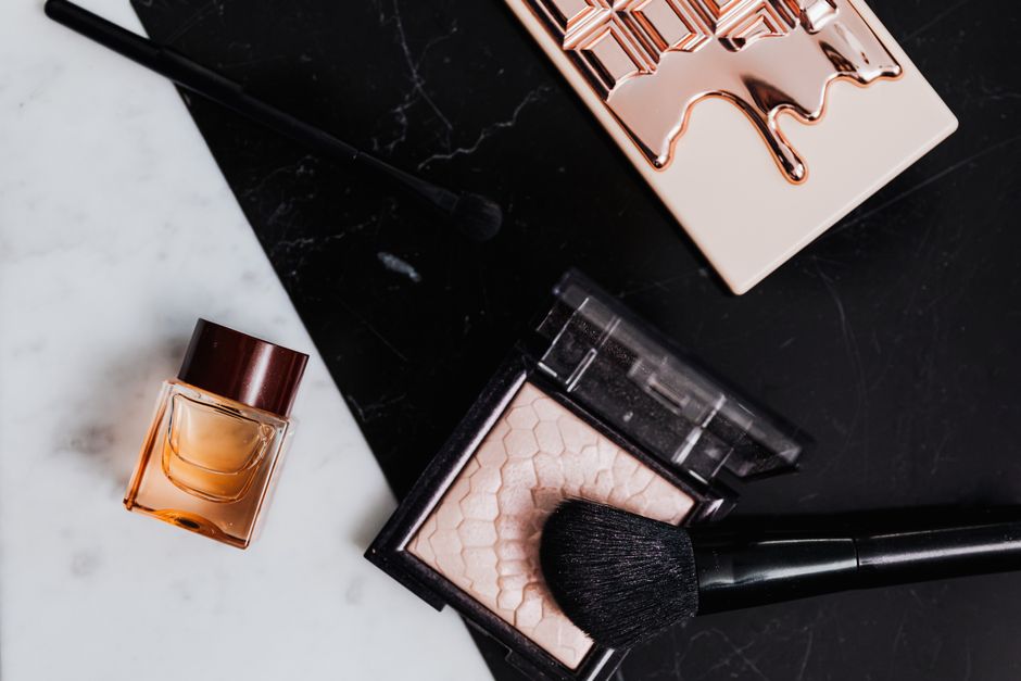 High-angle view of beauty products including eyeshadow, lipstick, and perfume on marble an