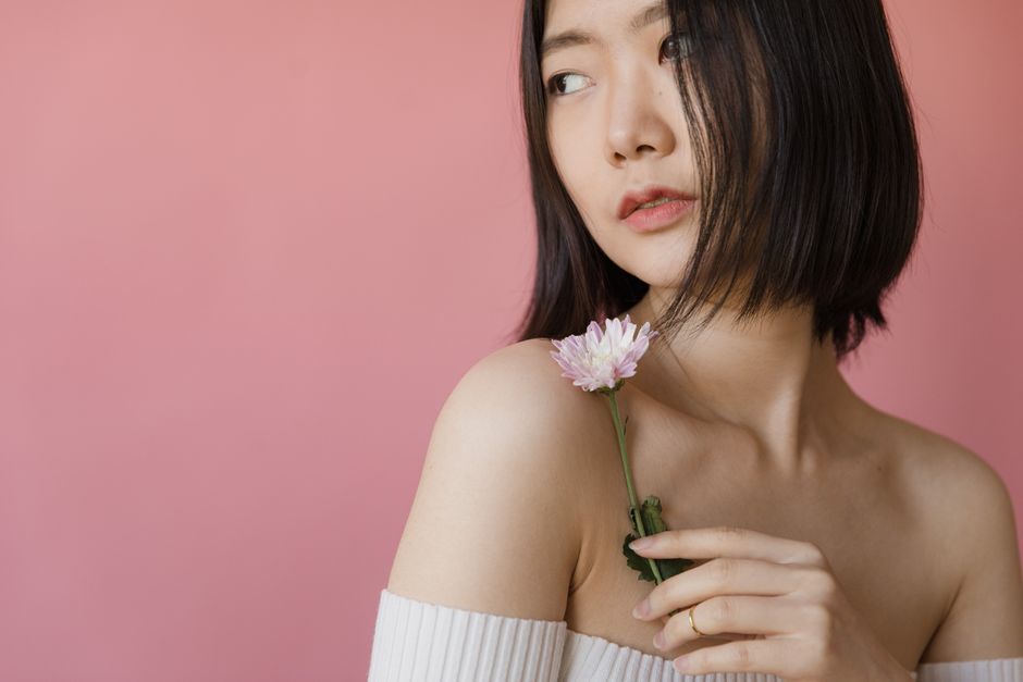A serene portrait of an Asian woman holding a flower against a pink background.