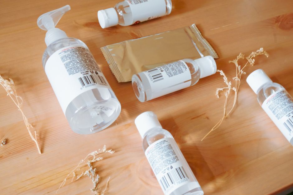 A close-up of hand sanitizer bottles and a sachet of wipes arranged on a wooden surface, conveying cleanliness and hygiene.