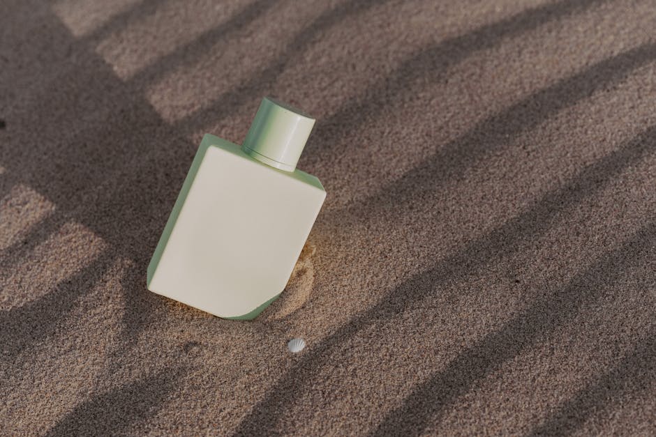 A minimalist perfume bottle partially buried in summer beach sand, casting artistic shadows.