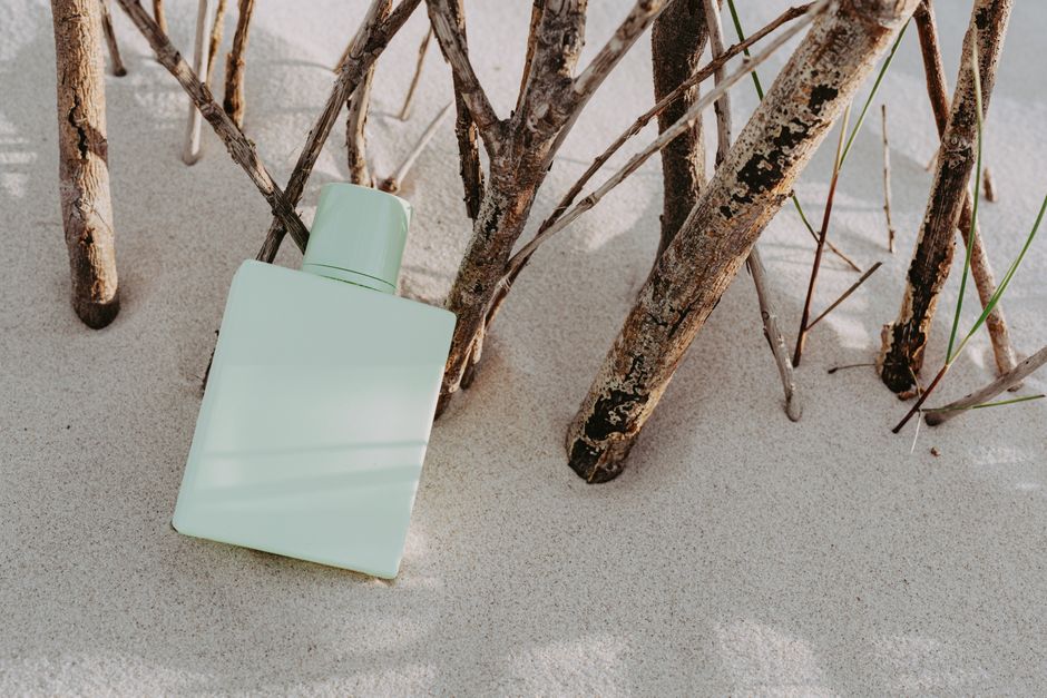A green perfume bottle artistically placed on sand amidst dry branches, creating a minimalist style.