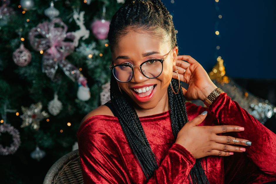 Joyful woman in a red dress with a Christmas tree background, celebrating the festive season.