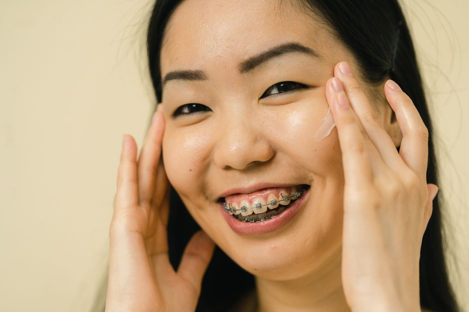 Close-up of a smiling woman with braces applying skincare cream, showcasing beauty and confidence.