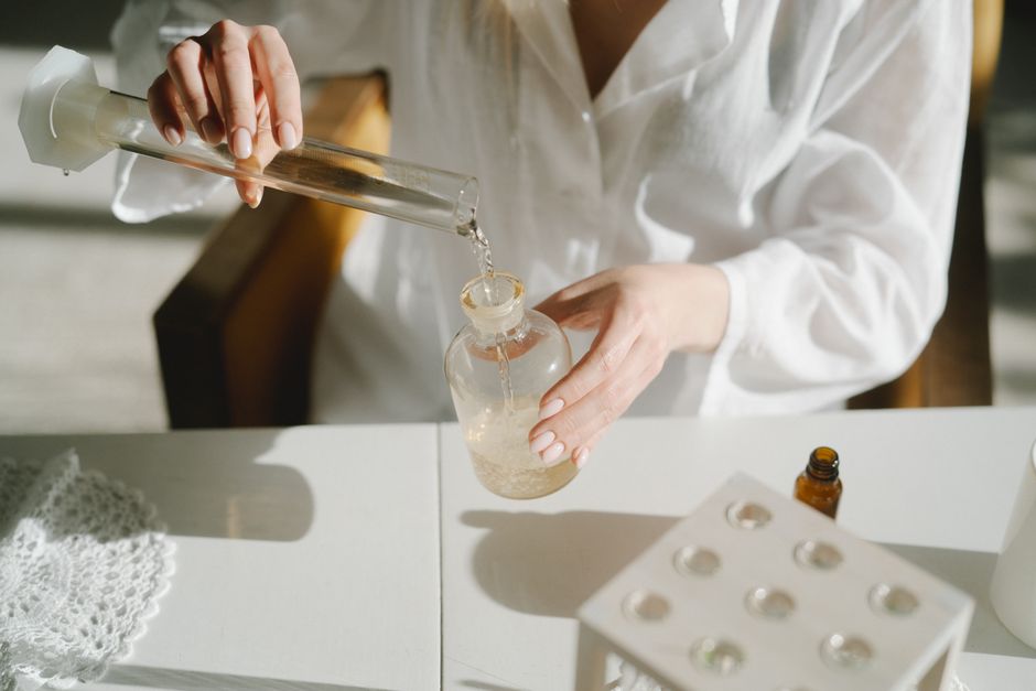 A scientist in white lab coat pours liquid between glass containers on a laboratory table.