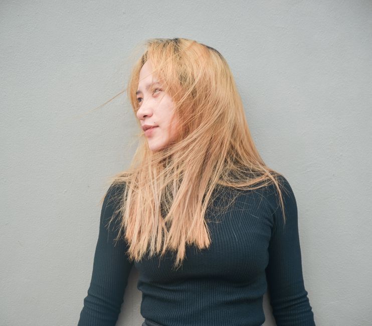 Stylish woman with flowing blonde hair poses against a simple gray background.