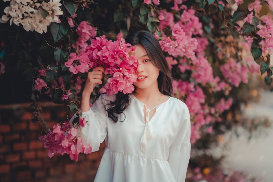 A woman in a white dress poses with vibrant pink bougainvillea flowers outdoors.