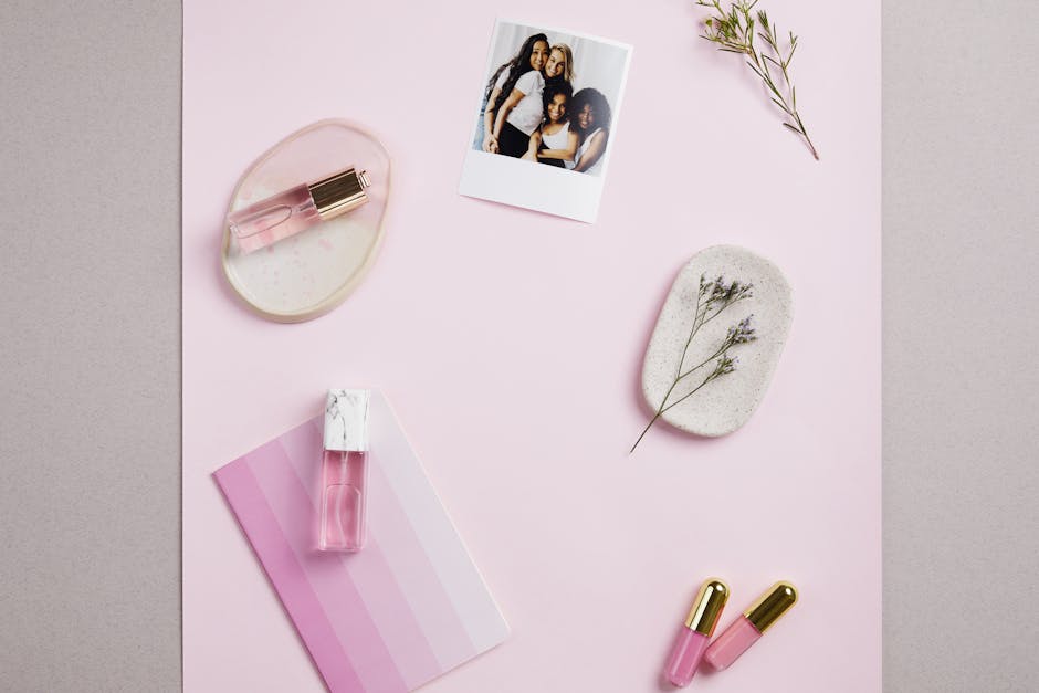 Stylish flat lay featuring pink-hued perfumes, floral decor, and a casual photograph on a soft pink backdrop.