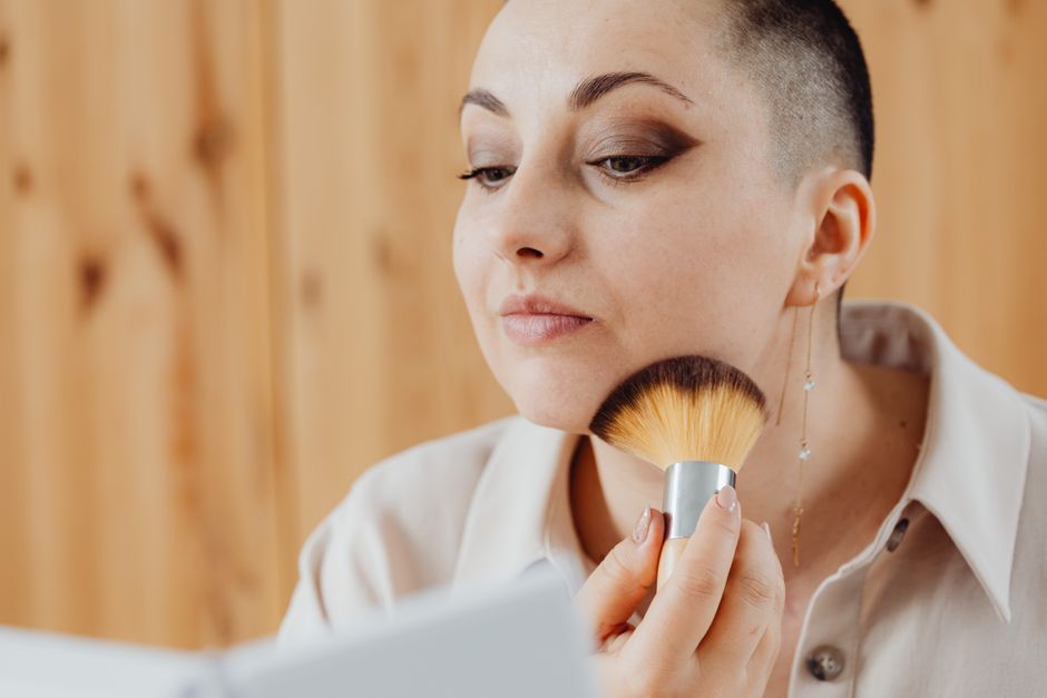 A woman carefully applies makeup using a soft brush in a warm indoor setting.