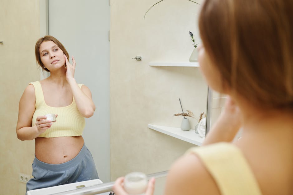 Pregnant woman using facial cream in bathroom mirror for skincare.