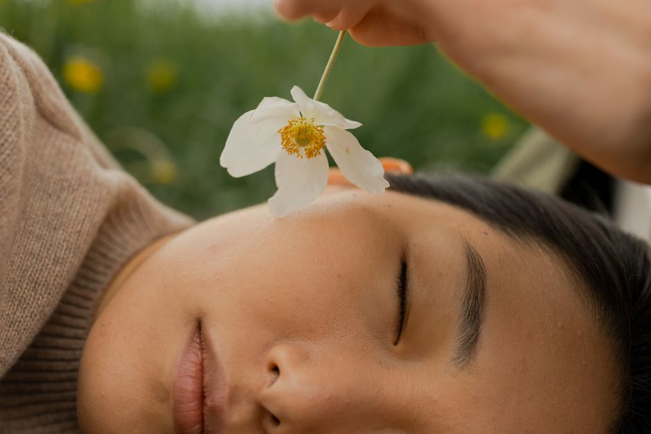 A serene moment outdoors with a playful touch of a flower on a woman's face.